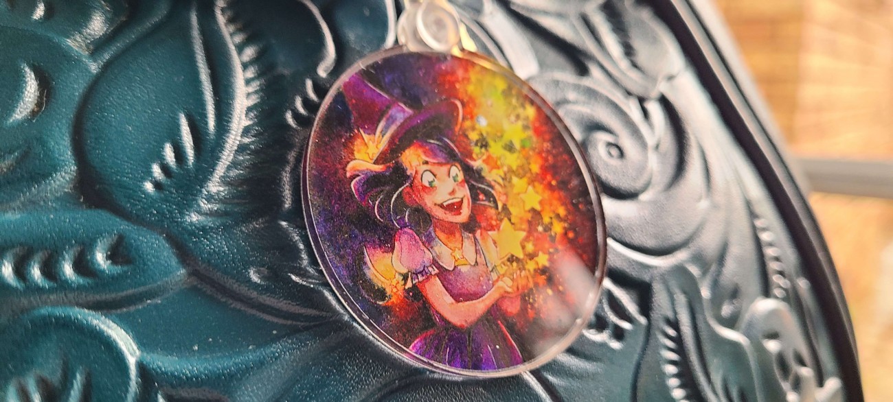 Colorful acrylic charm featuring a young witch creating stars out of magic