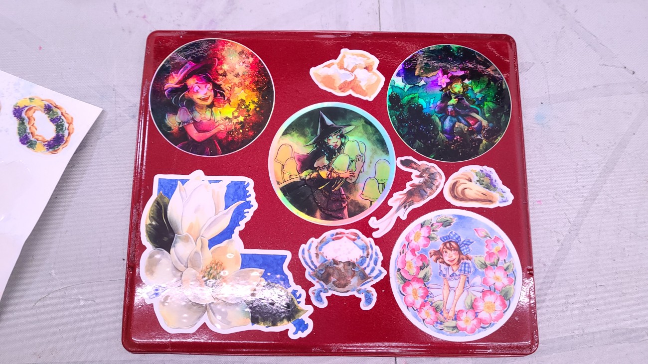 A bunch of stickers on my custom watercolor palette.  Top left is the Starry Witch holographic sticker.