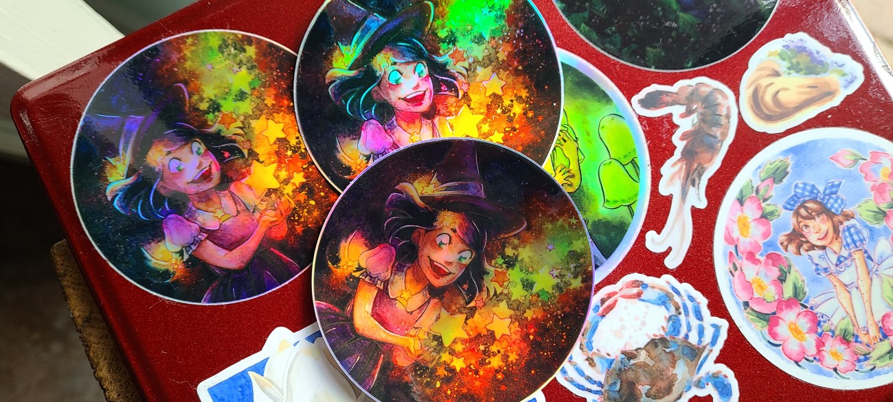 A shiny, shimmering holographic sticker of a young witch casting some colorful star magic.